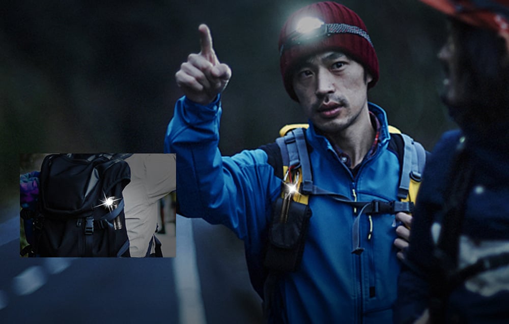 A man in a blue jacket pointing forward. He wears a red cap and a Superfire TH04 headlamp.