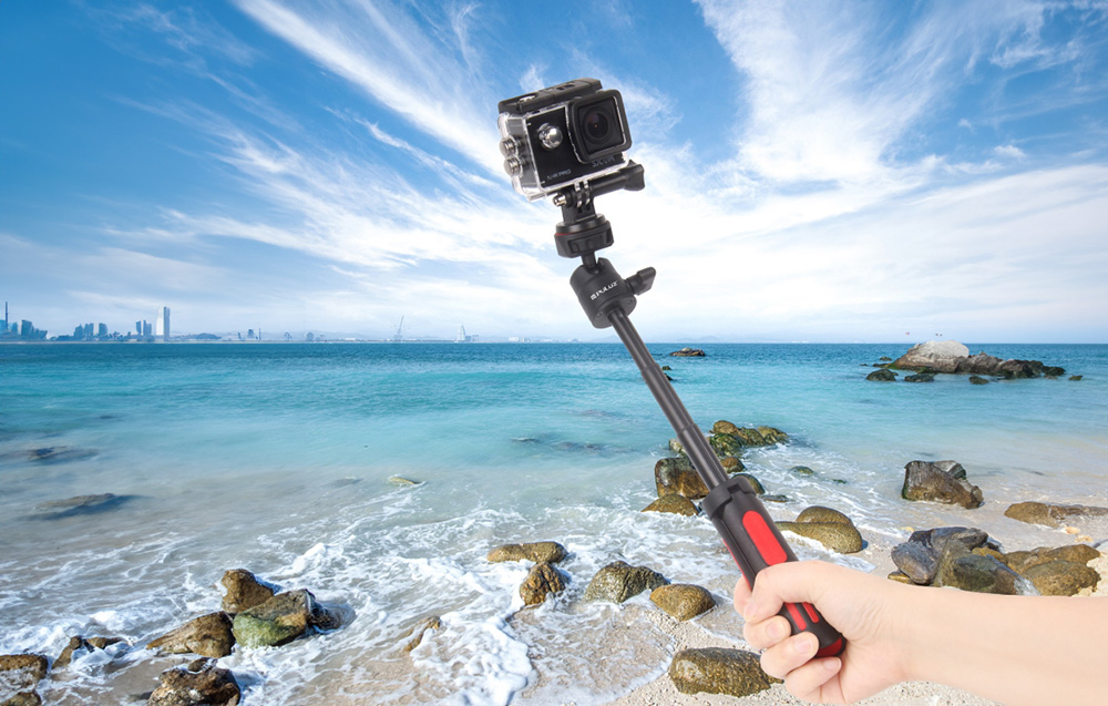 Hand holding PULUZ selfie stick with action camera against sea background